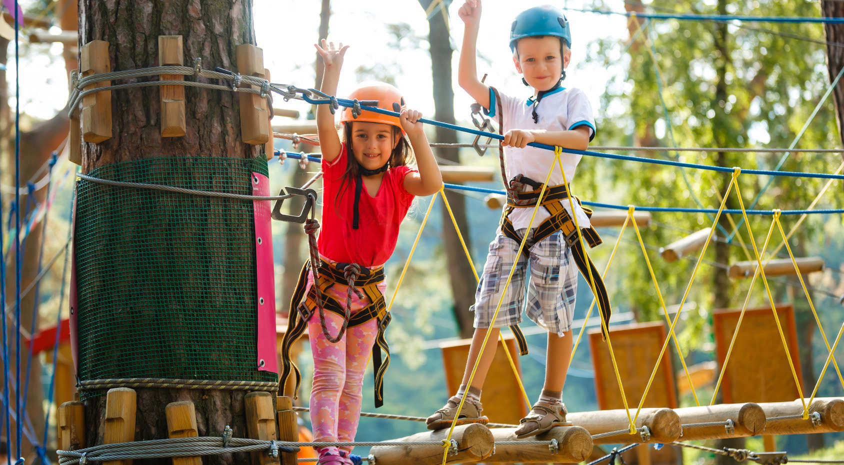 Niños con casco y arnés en circuito de aventura entre árboles