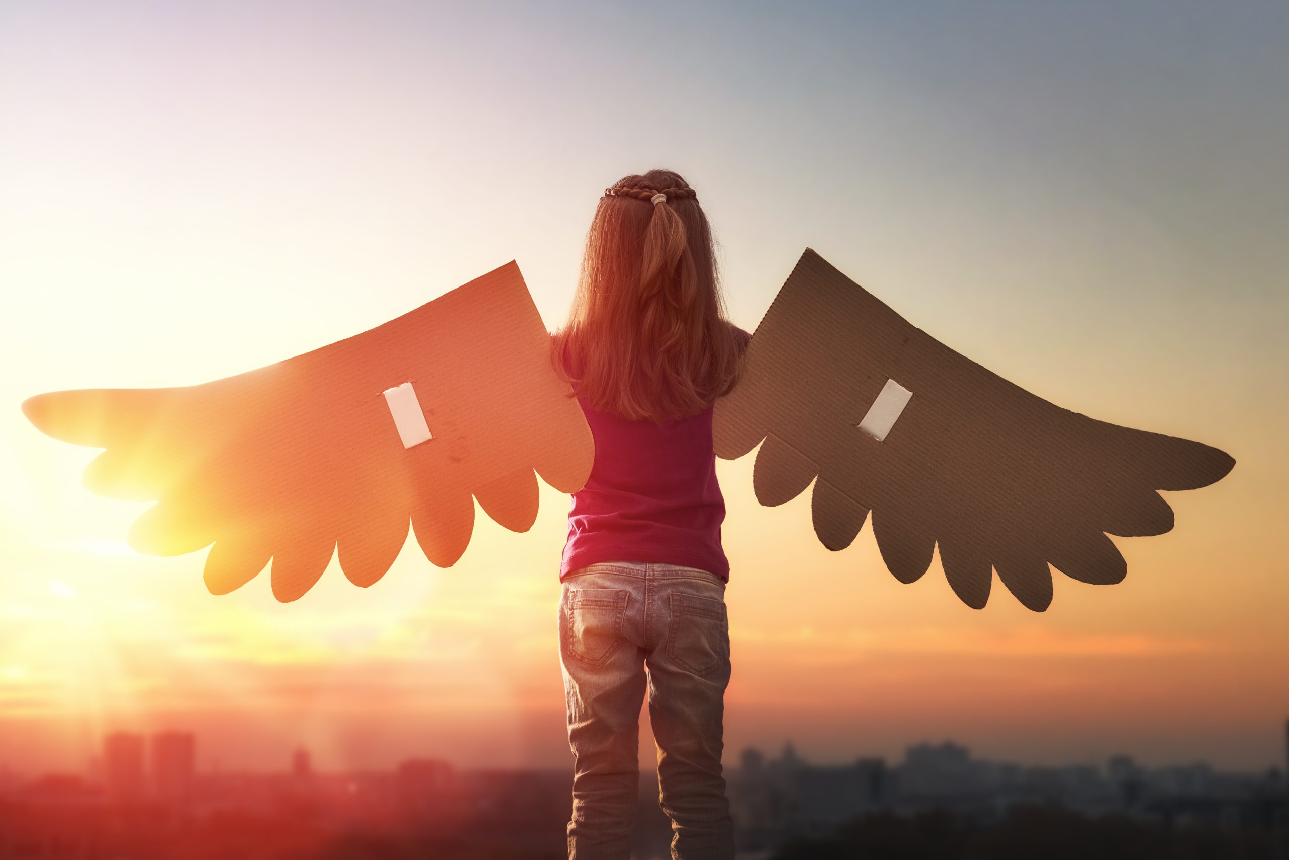 Niña con alas de cartón mirando el horizonte al atardecer