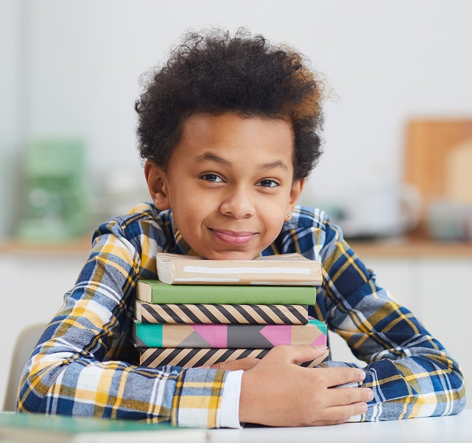 niño apoyado en una pila de libros sonriendo