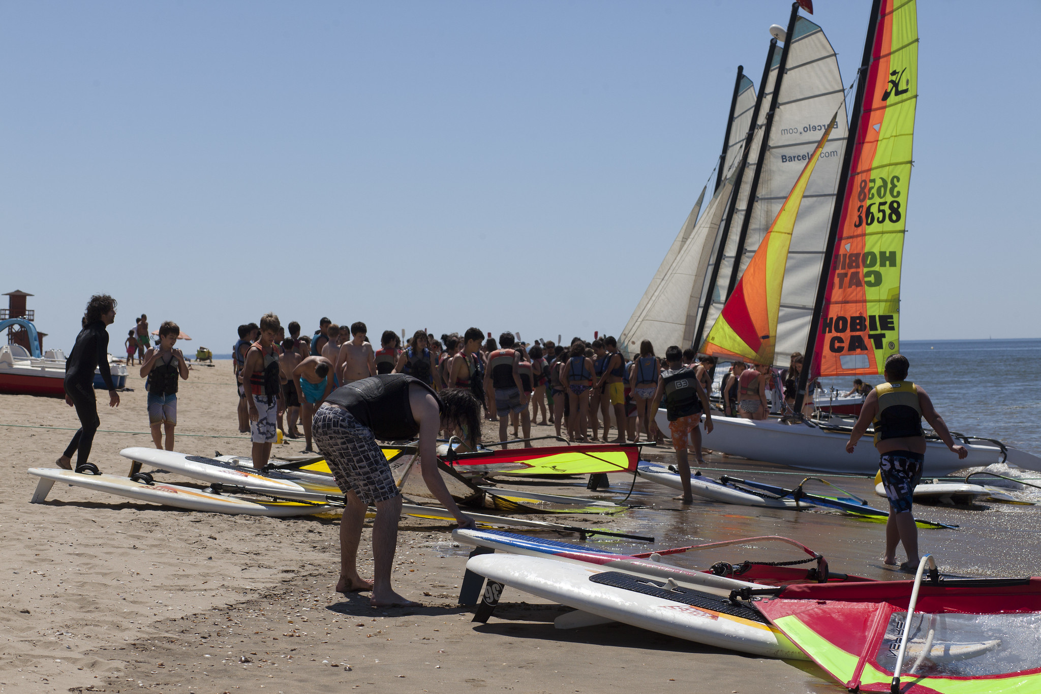 jóvenes y catamaranes en la orilla preparando actividad náutica