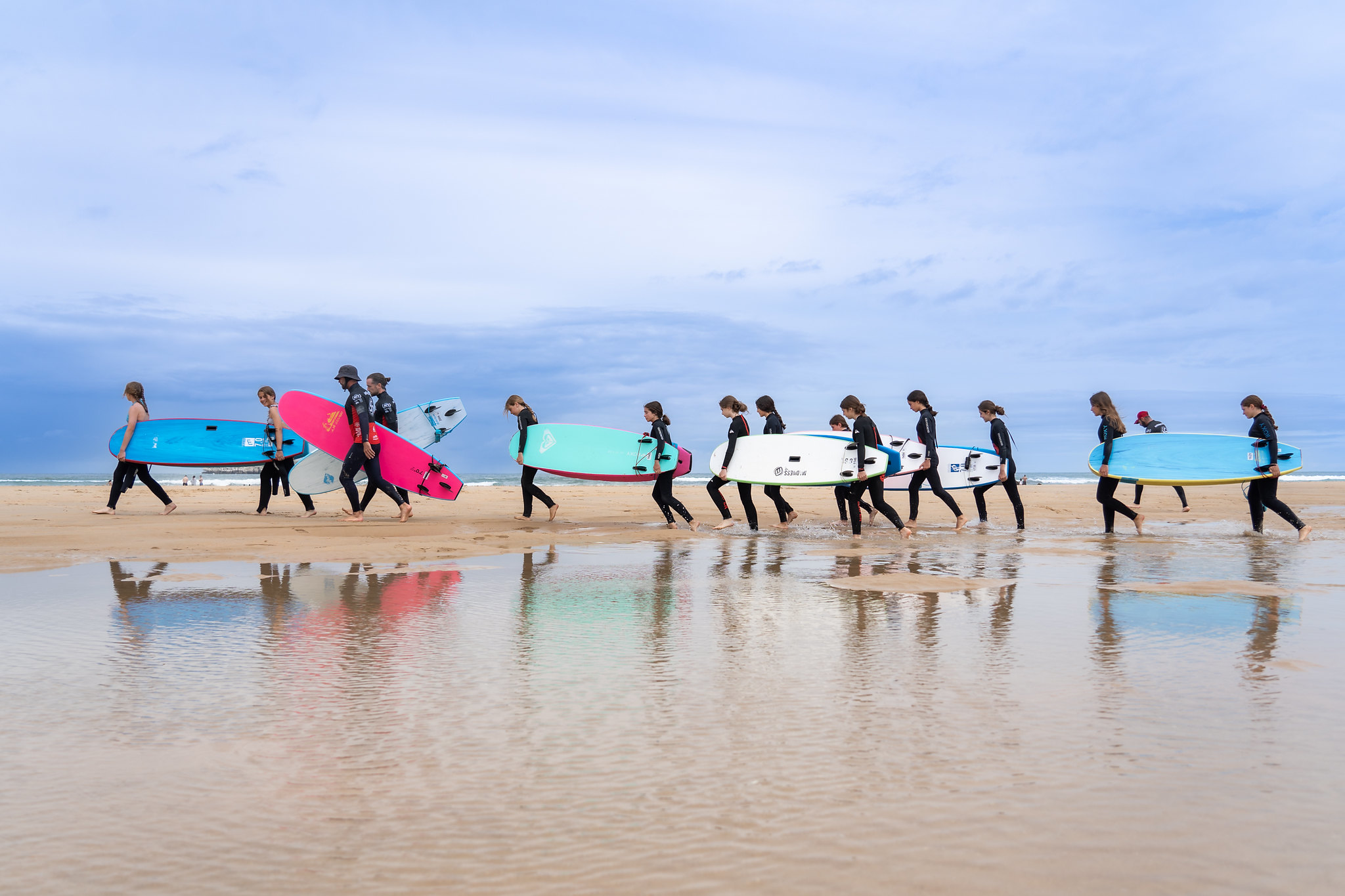 fila de jóvenes caminando por la playa con tablas de surf
