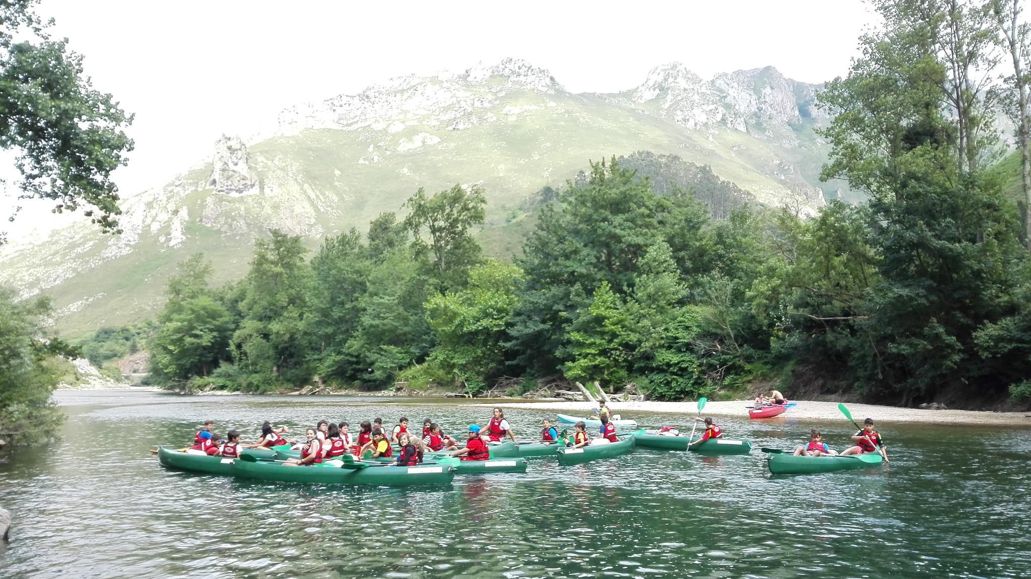 niños en canoas remando por río con montañas al fondo