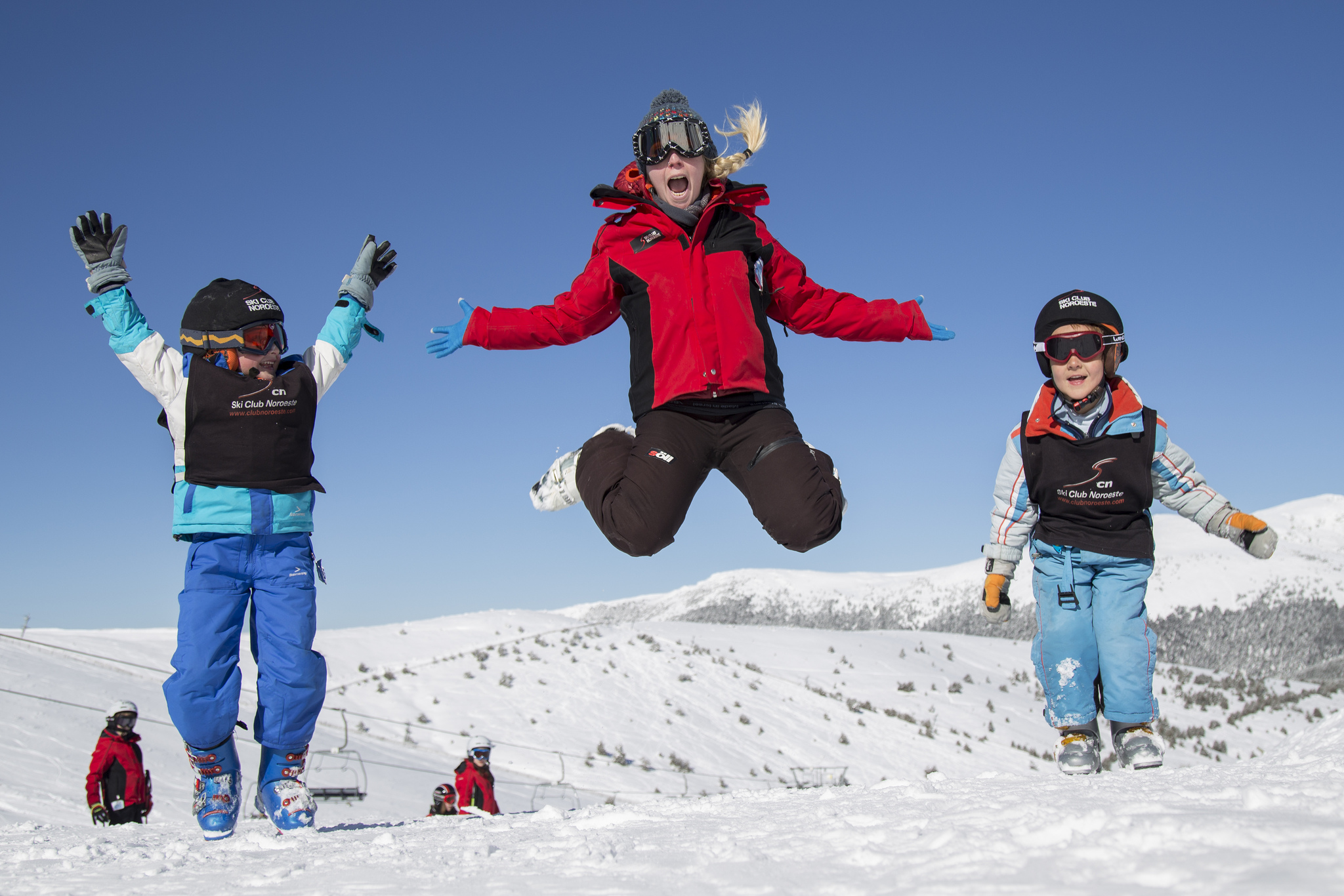 Niños con equipación de esquí saltando en la nieve durante un viaje escolar