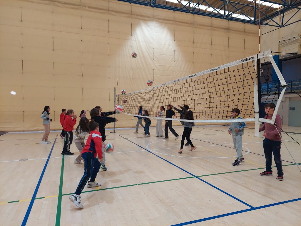 niños jugando al voleibol en pabellón deportivo