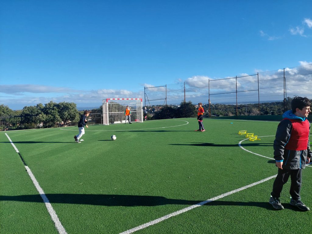 niños jugando al fútbol en campo de hierba artificial
