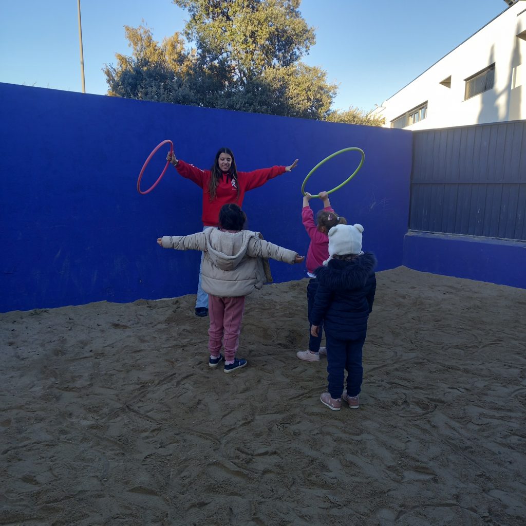 monitora y niños jugando con aros en patio de arena