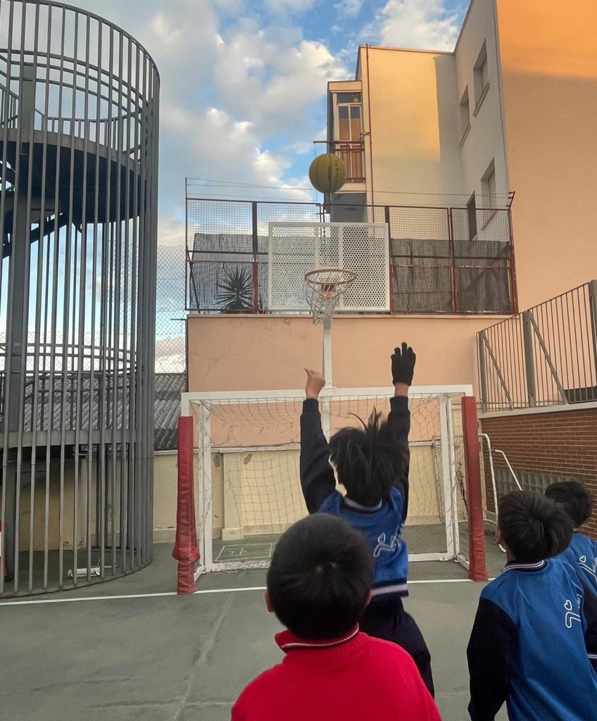 niño lanzando a canasta en pista exterior del colegio