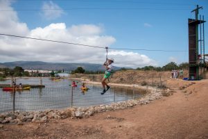 joven en tirolina sobre lago con kayaks al fondo