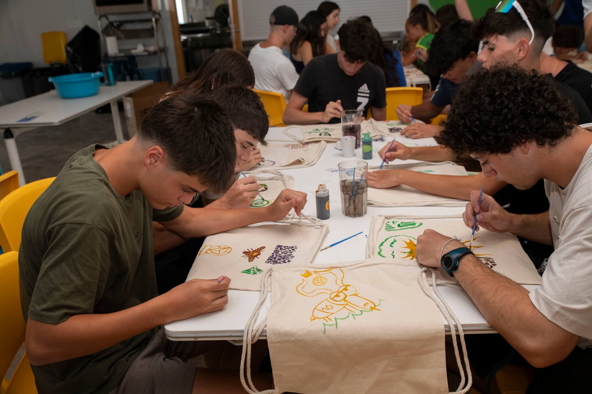 jóvenes pintando bolsas de tela en taller de manualidades